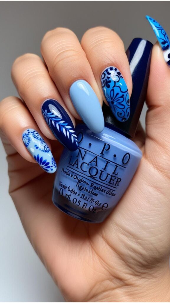 Hand with blue nail designs, showcasing various shades of blue and design variations.